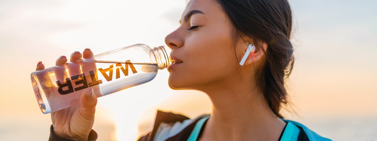 bere acqua ogni ora per accelerare il metabolismo ragazza sportiva al tramonto mentre beve acqua e ascolta musica