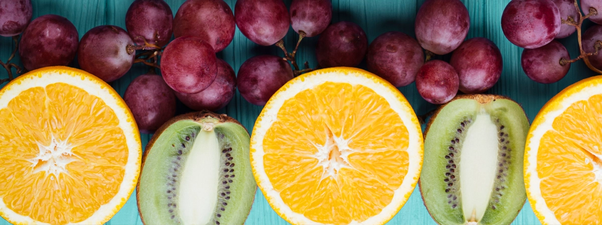 Liberare l'organismo dai radicali liberi Resveratrolo Vitamica C antiossidanti uva arance kiwi su tavolo azzurro